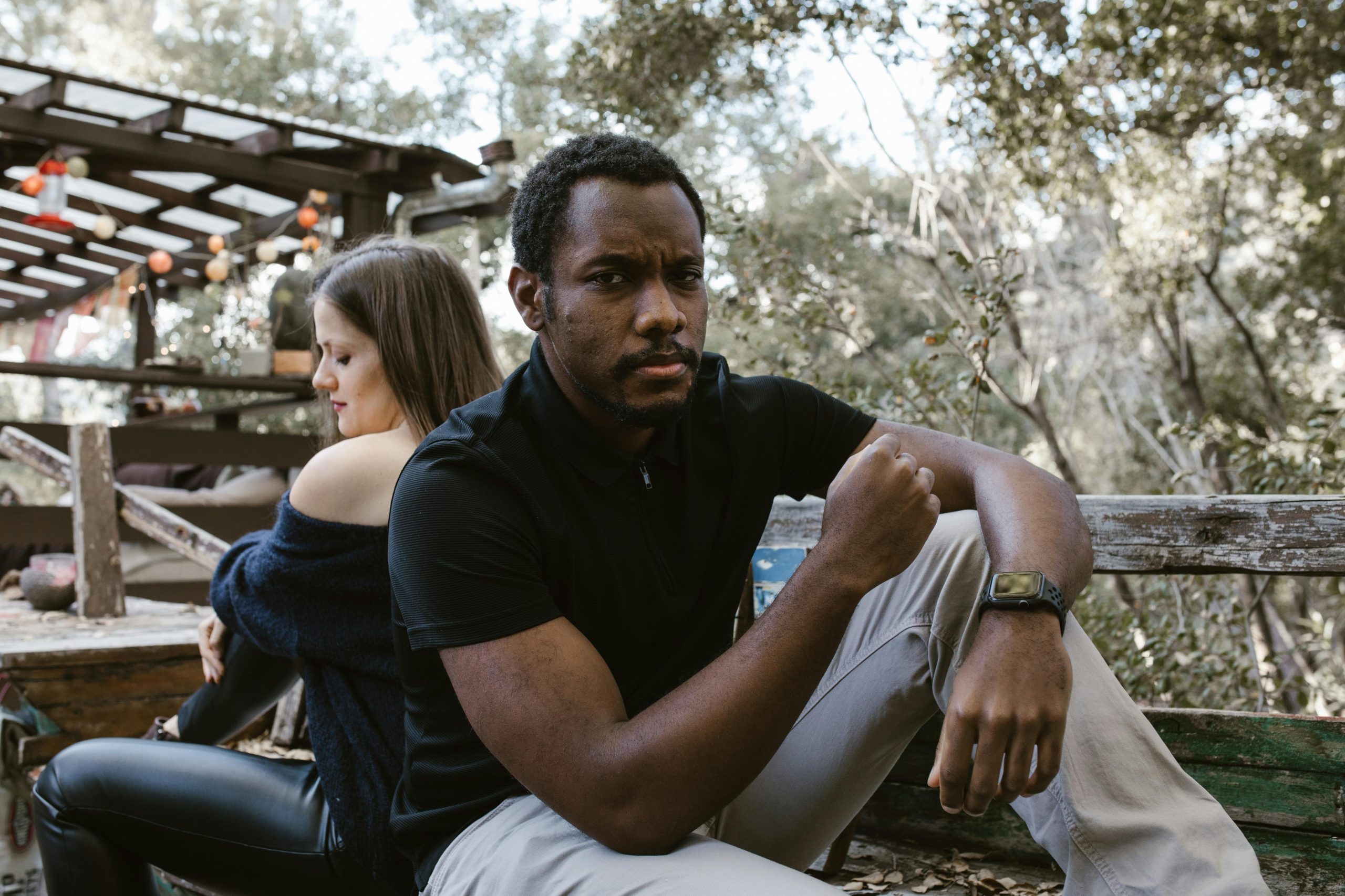 Un homme pensif assis à l'extérieur, avec une femme assise à distance derrière lui.
