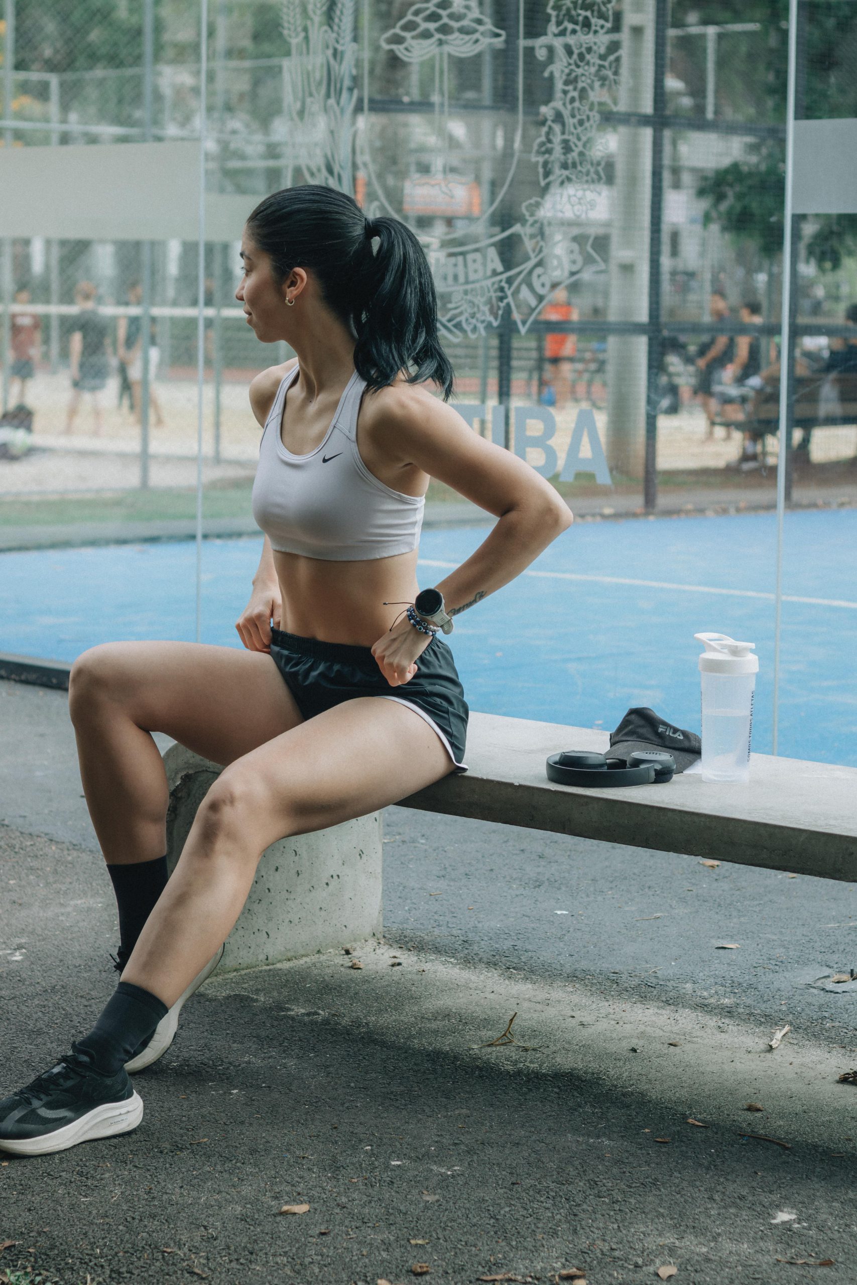Une athlète féminine faisant une pause sur un banc en extérieur. Cadre sportif en pleine journée ensoleillée.