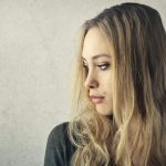 Une jeune femme pensive aux longs cheveux blonds regardant sur le côté sur un fond neutre.