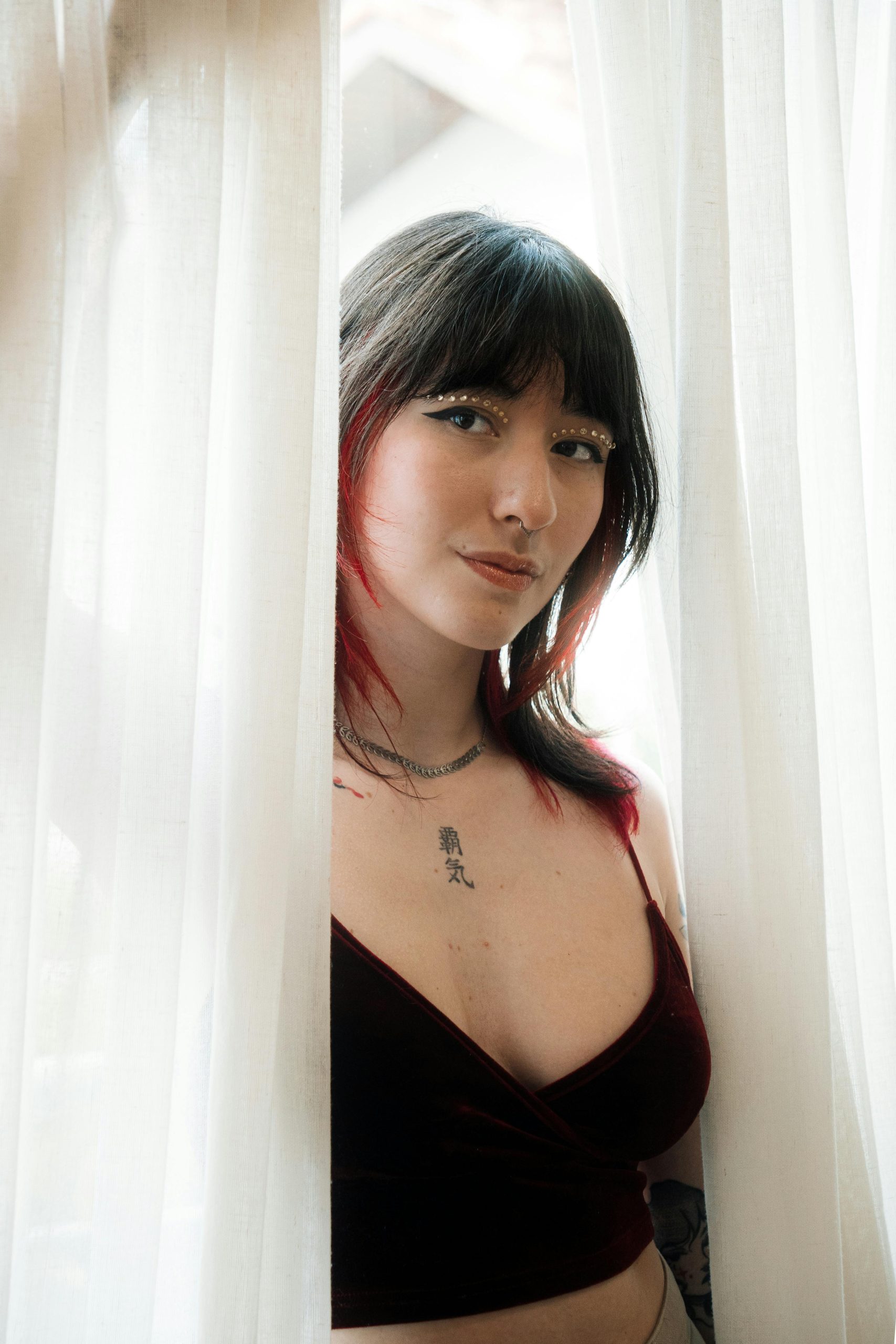 Elegant portrait d'une femme avec des tatouages apparaissant à travers des rideaux blancs.