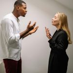 Un couple en pleine dispute animée à l'intérieur, exprimant des émotions fortes et des gestes.