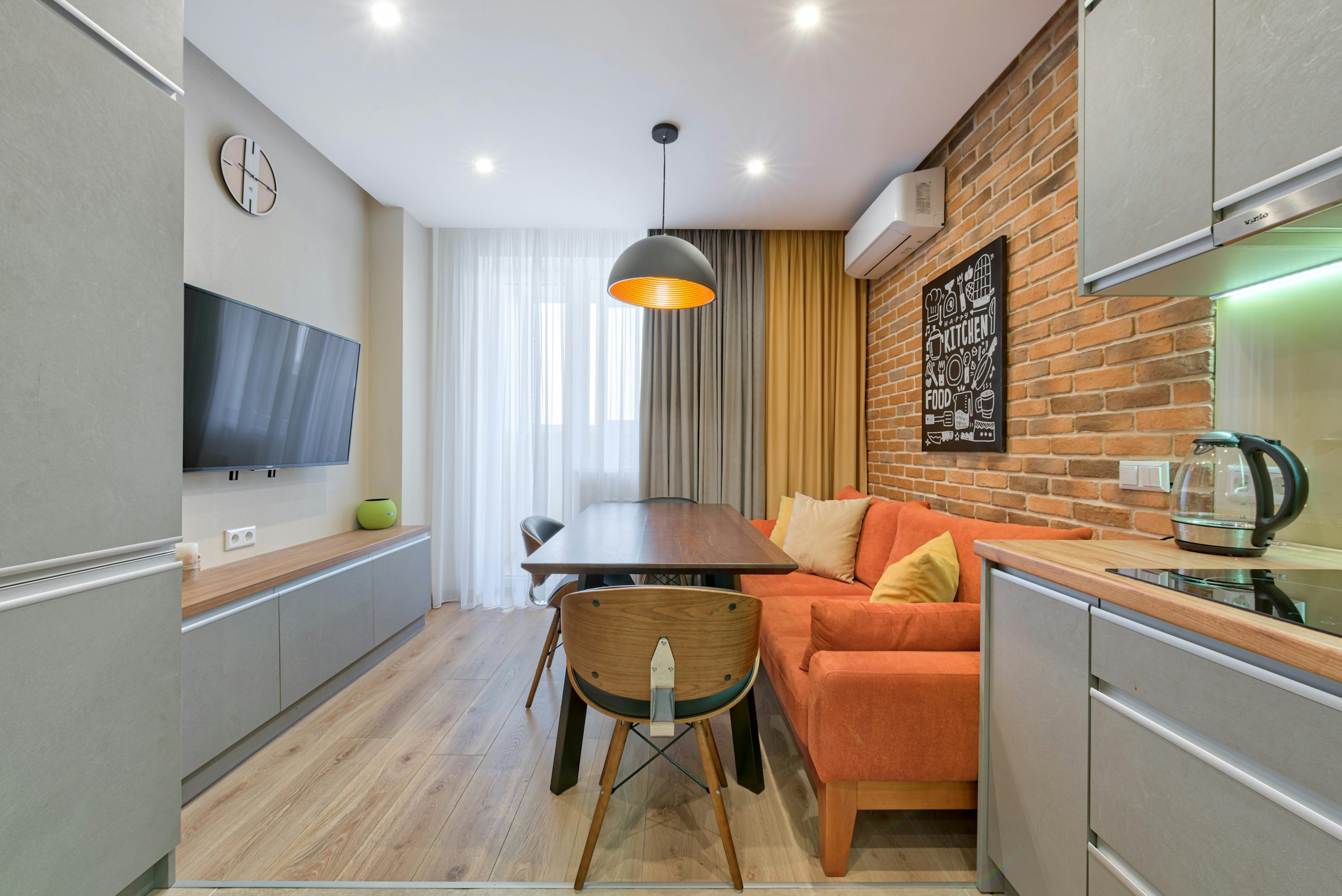 Stylish apartment interior avec un mur en briques, un canapé orange et des meubles en bois