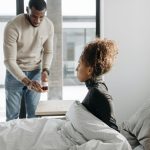 A man provides support to a sick woman in a cozy, indoor setting. Un homme soutient une femme malade dans un cadre intérieur confortable.