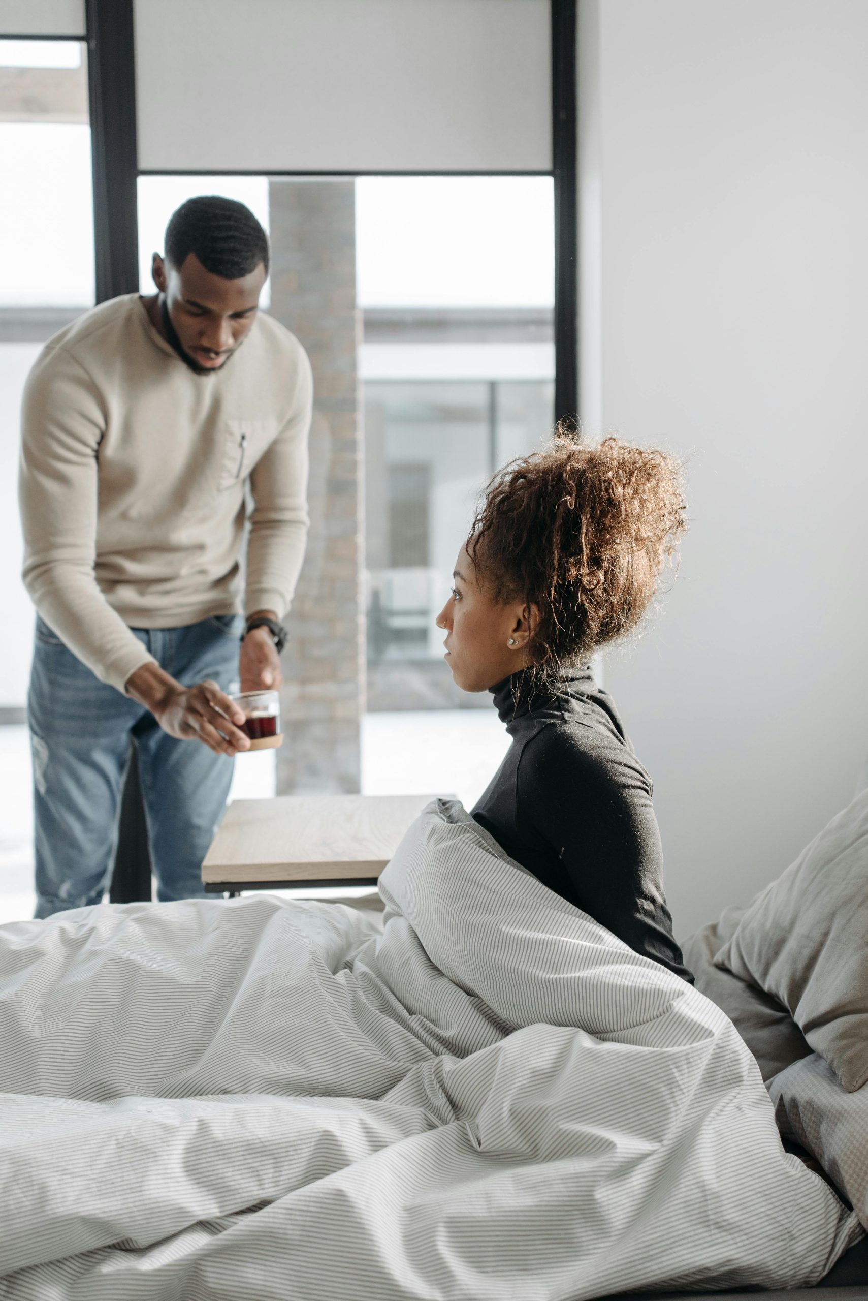 A man provides support to a sick woman in a cozy, indoor setting. Un homme soutient une femme malade dans un cadre intérieur confortable.