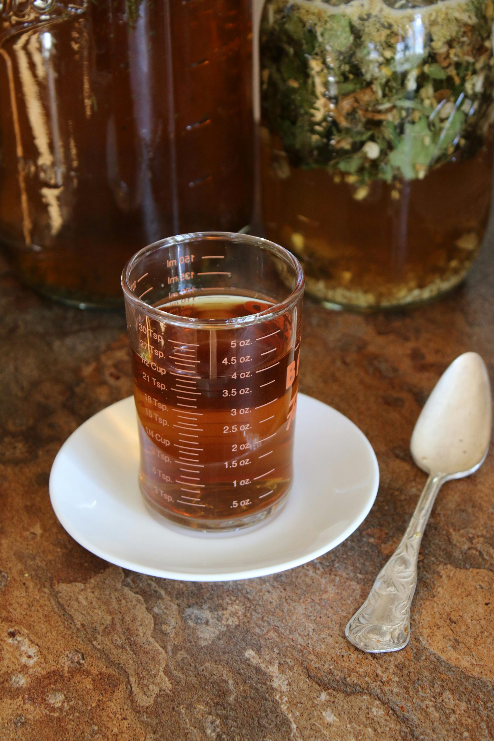 Aromatique infusion aux herbes dans un verre doseur sur une soucoupe avec des bocaux en arrière-plan.