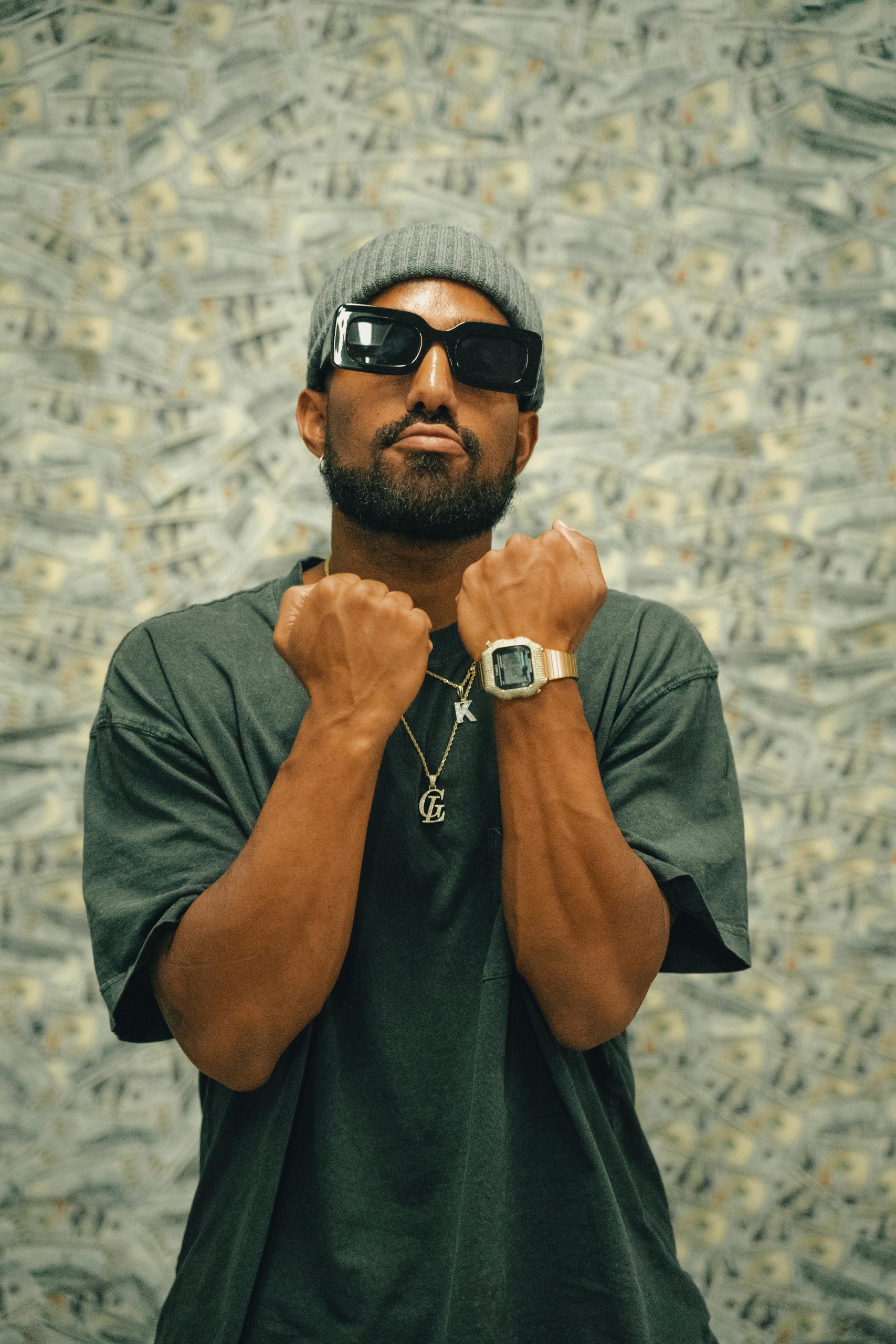 Stylish man en lunettes de soleil et bijoux pose avec confiance, mettant en valeur la mode urbaine moderne.