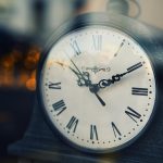 Close-up of a vintage clock with Roman numerals, softly lit background. Gros plan d'une horloge vintage avec des chiffres romains, arrière-plan doucement éclairé.