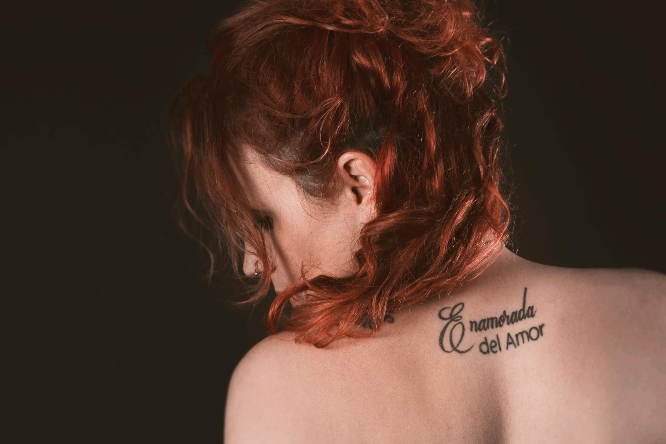 Artistic portrait of a redhead woman with back tattoo in a studio setting. Portrait artistique d'une femme rousse avec un tatouage dans le dos dans un cadre de studio.