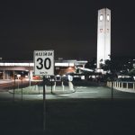 A city street at night featuring a speed limit sign and an illuminated clock tower, creating an urban atmosphere. Une rue de ville la nuit avec un panneau de limitation de vitesse et une tour d'horloge illuminée, créant une atmosphère urbaine.