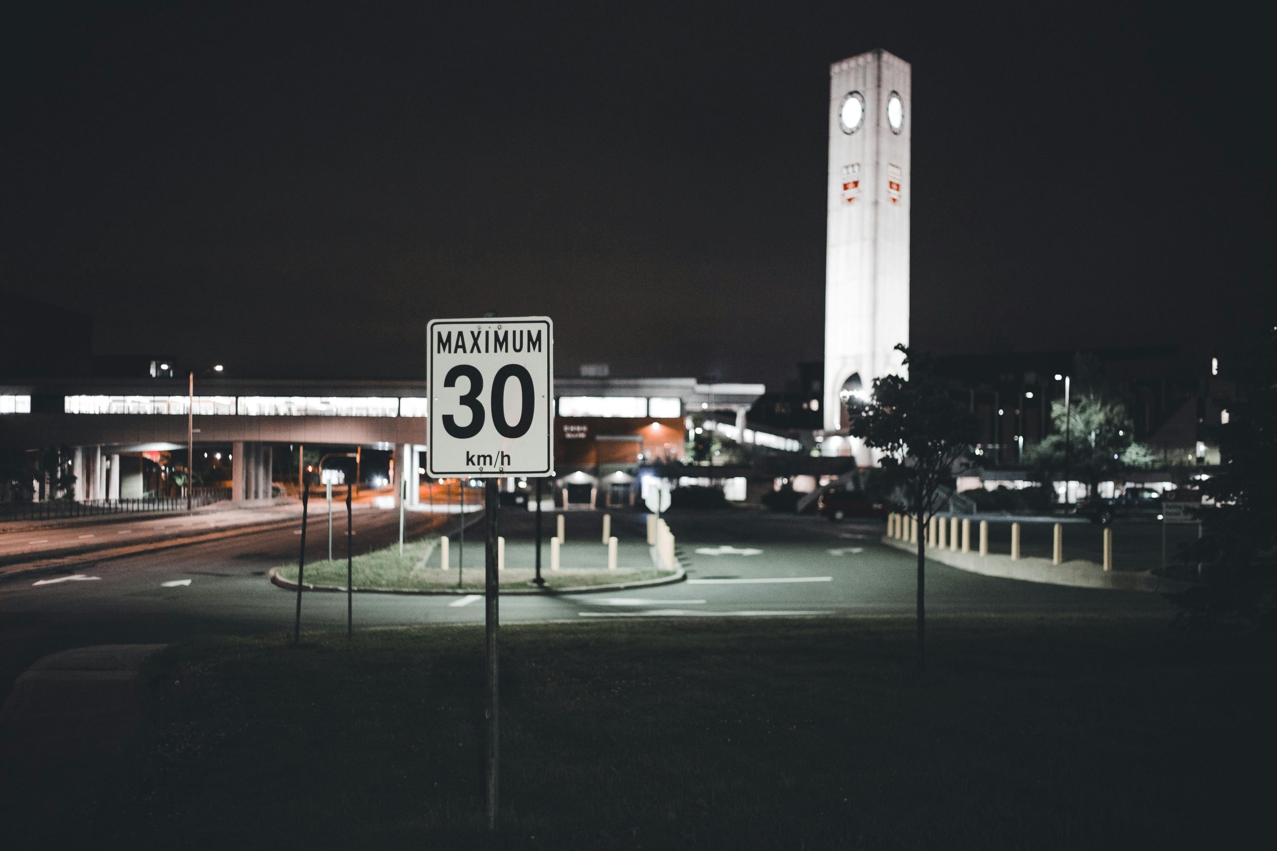 A city street at night featuring a speed limit sign and an illuminated clock tower, creating an urban atmosphere. Une rue de ville la nuit avec un panneau de limitation de vitesse et une tour d'horloge illuminée, créant une atmosphère urbaine.