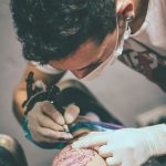 Artiste tatoueur concentré intensément sur la création d'un tatouage détaillé à la jambe dans un cadre de studio.