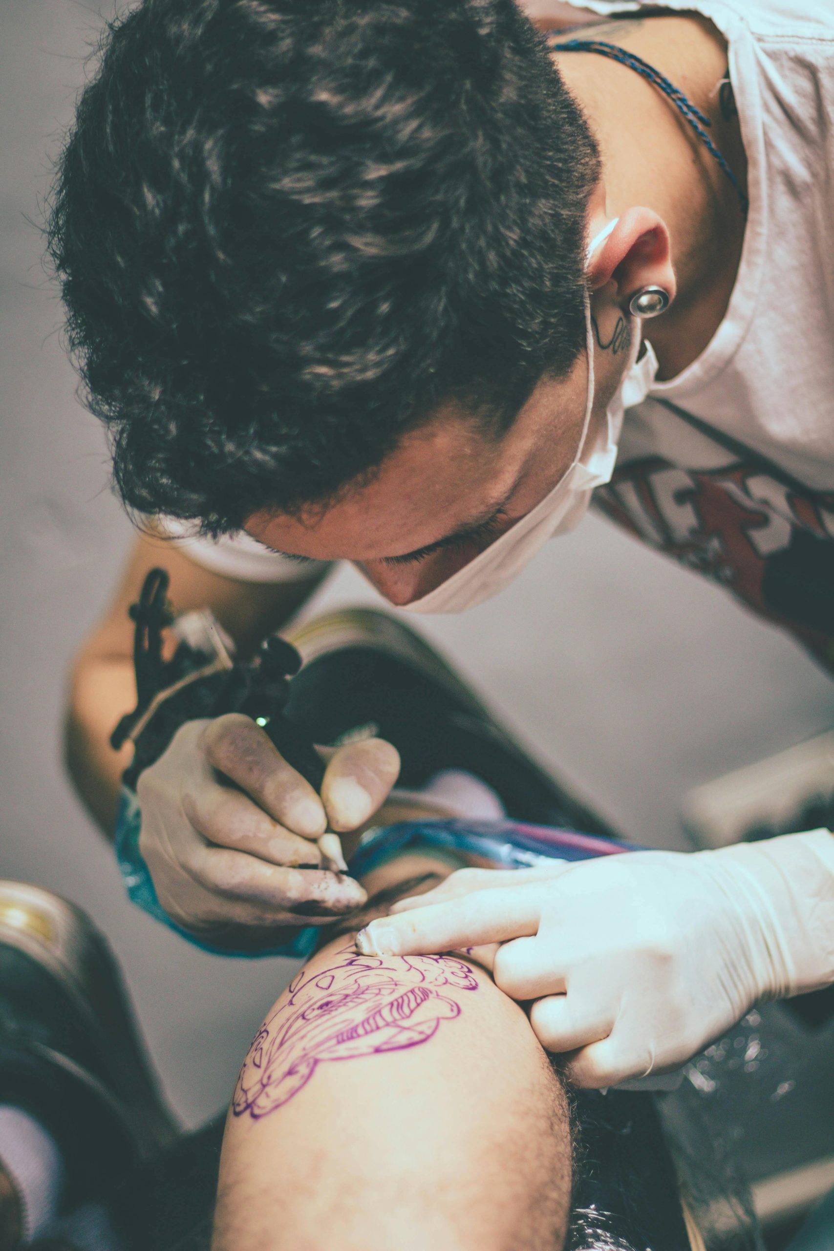 Artiste tatoueur concentré intensément sur la création d'un tatouage détaillé à la jambe dans un cadre de studio.