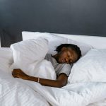 An adult sleeping peacefully on a bed with white pillows and linen. Un adulte dormant paisiblement sur un lit avec des oreillers et du linge blanc.