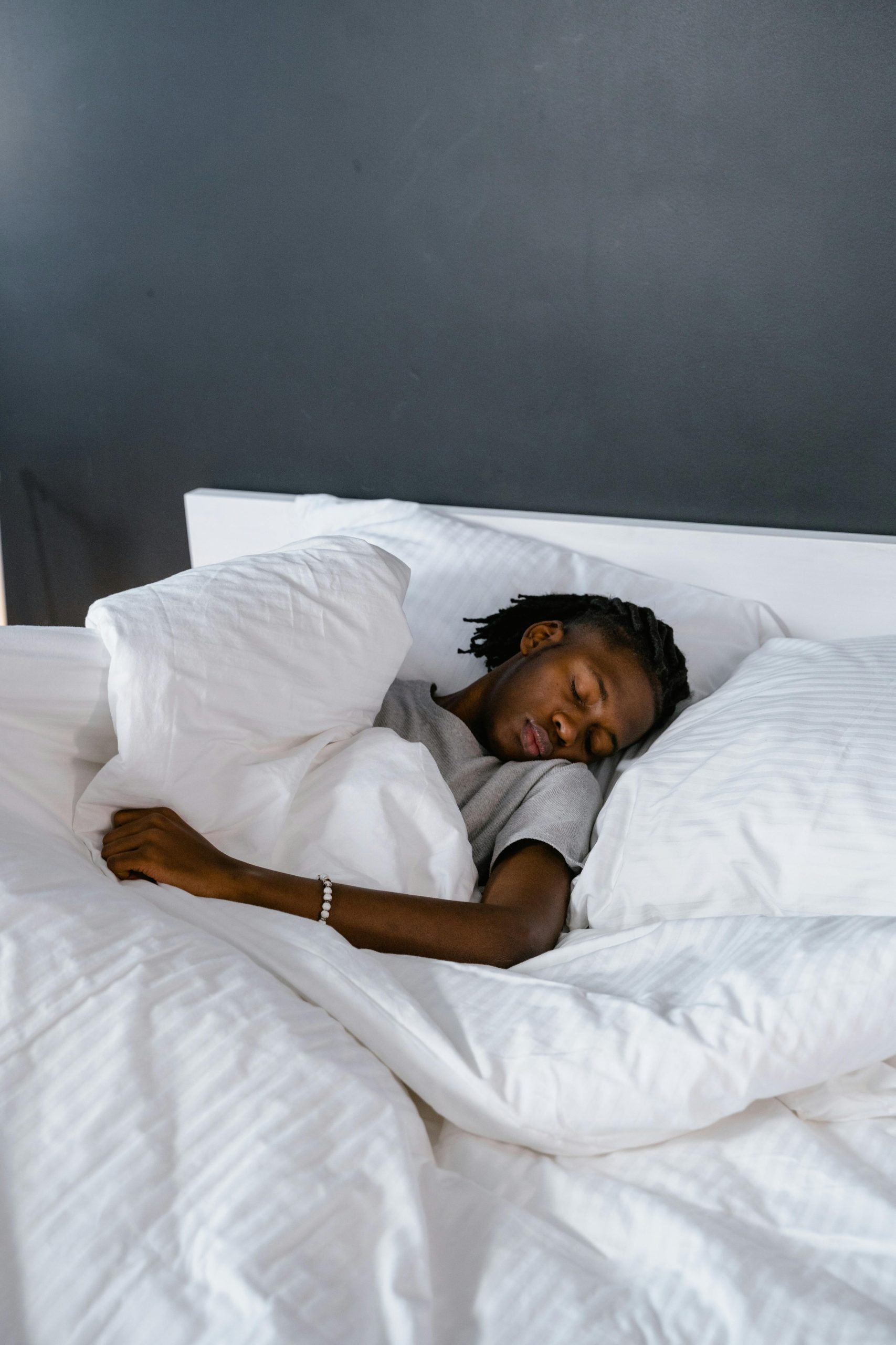 An adult sleeping peacefully on a bed with white pillows and linen. Un adulte dormant paisiblement sur un lit avec des oreillers et du linge blanc.