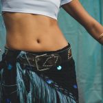 Close-up of a woman's belly with stylish jewelry and bohemian attire in a dance pose. Gros plan du ventre d'une femme avec des bijoux élégants et une tenue bohème en pose de danse.