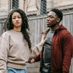 Sad ethnic girlfriend with curly hair rejecting annoyed African American boyfriend while arguing on street near wooden fence during breakup Petite amie ethnique triste aux cheveux bouclés rejetant un petit ami afro-américain ennuyé en se disputant dans la rue près d'une clôture en bois pendant une rupture