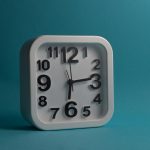Square white wall clock displaying 10:10 against a blue backdrop, perfect for minimalistic and modern design themes. Horloge murale blanche carrée affichant 10:10 sur un fond bleu, parfaite pour les thèmes de design minimaliste et moderne.