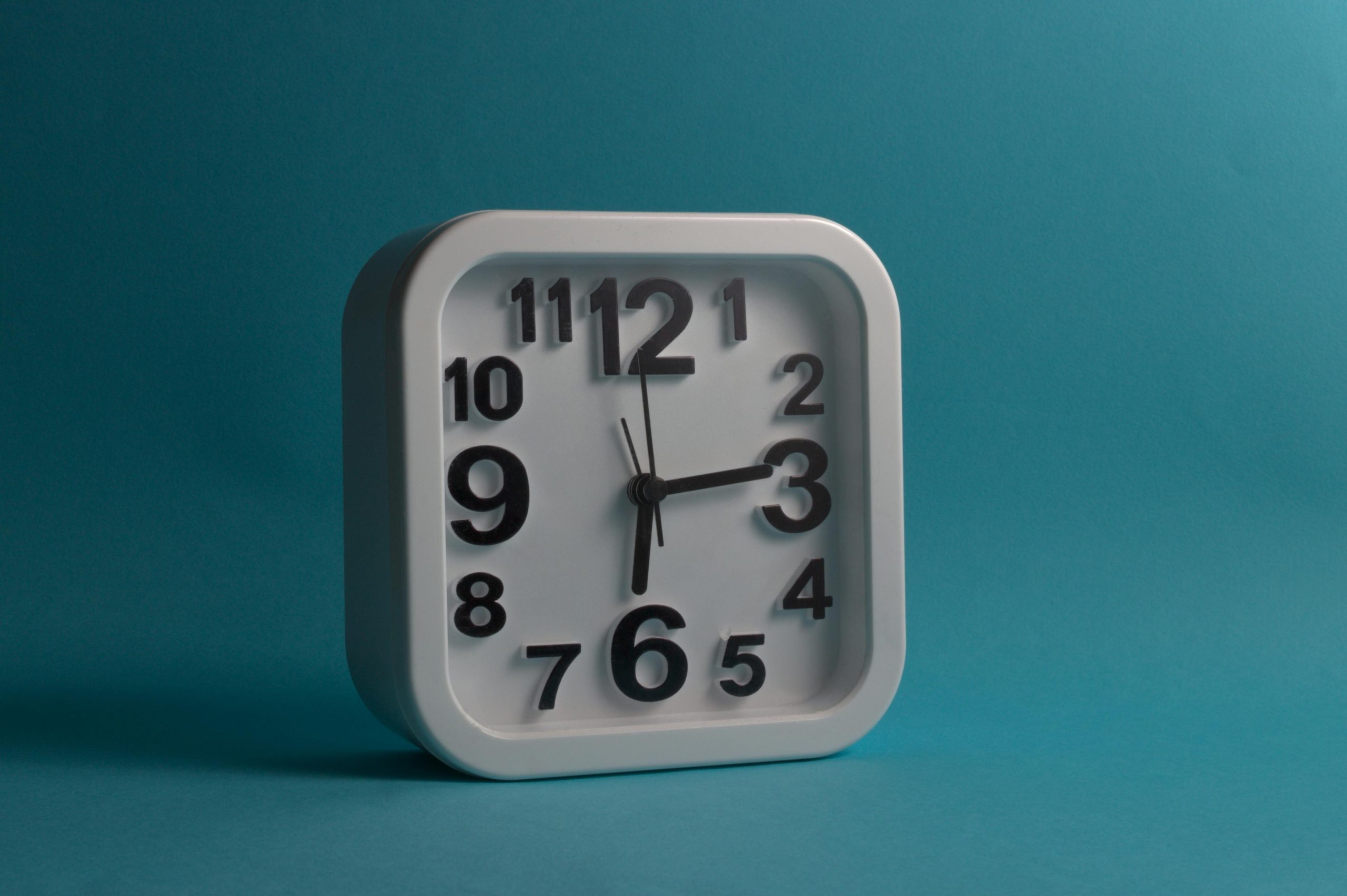 Square white wall clock displaying 10:10 against a blue backdrop, perfect for minimalistic and modern design themes. Horloge murale blanche carrée affichant 10:10 sur un fond bleu, parfaite pour les thèmes de design minimaliste et moderne.