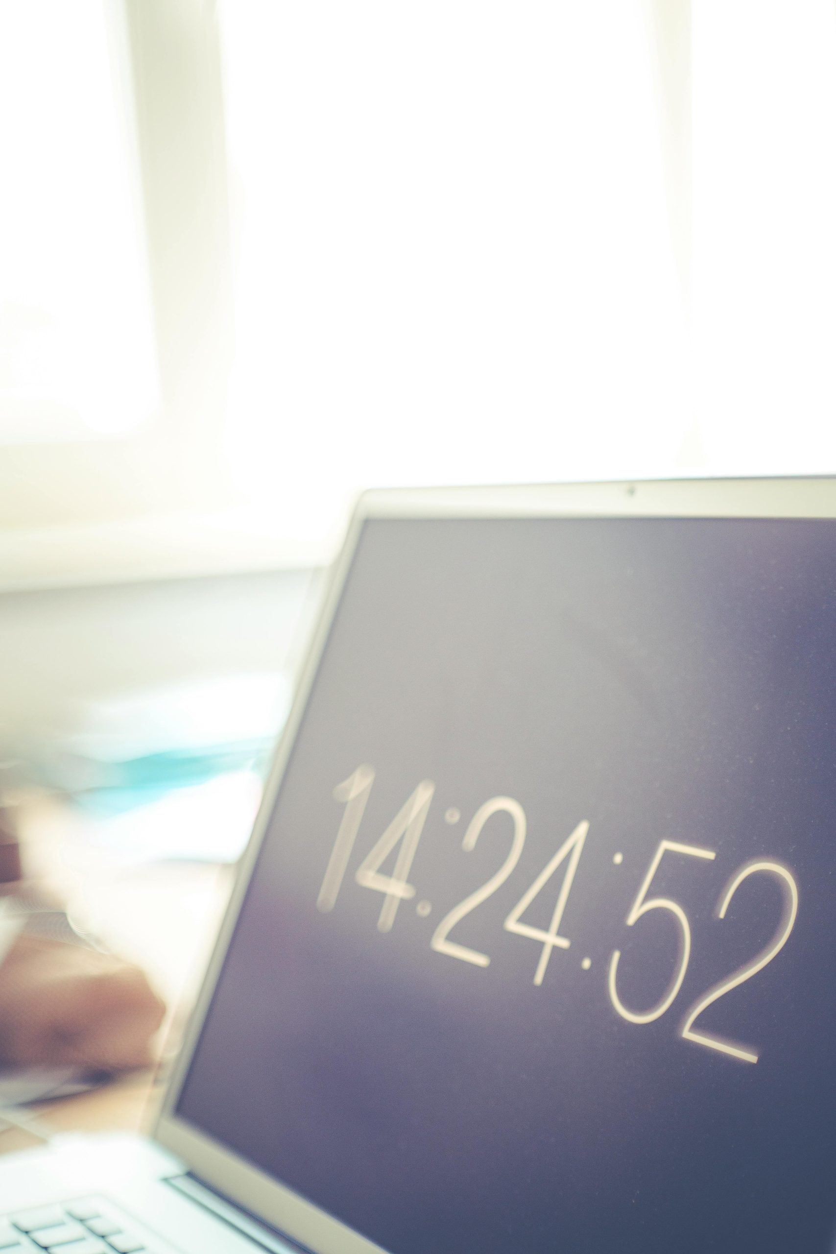 Laptop screen showing digital clock with blurred bright office background. Écran d'ordinateur portable affichant une horloge numérique avec un arrière-plan de bureau flou et lumineux.