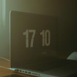 A dimly lit workspace featuring a laptop displaying the time and a smartphone on the table. Un espace de travail faiblement éclairé avec un ordinateur portable affichant l'heure et un smartphone sur la table.