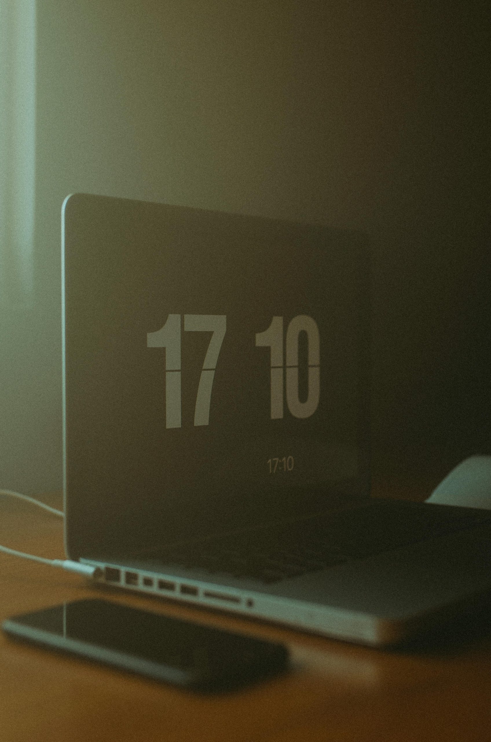 A dimly lit workspace featuring a laptop displaying the time and a smartphone on the table. Un espace de travail faiblement éclairé avec un ordinateur portable affichant l'heure et un smartphone sur la table.