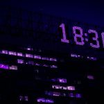 A modern building is illuminated at night with a prominent digital clock showing 18:30. Un bâtiment moderne illuminé la nuit avec une horloge numérique bien en vue affichant 18:30.