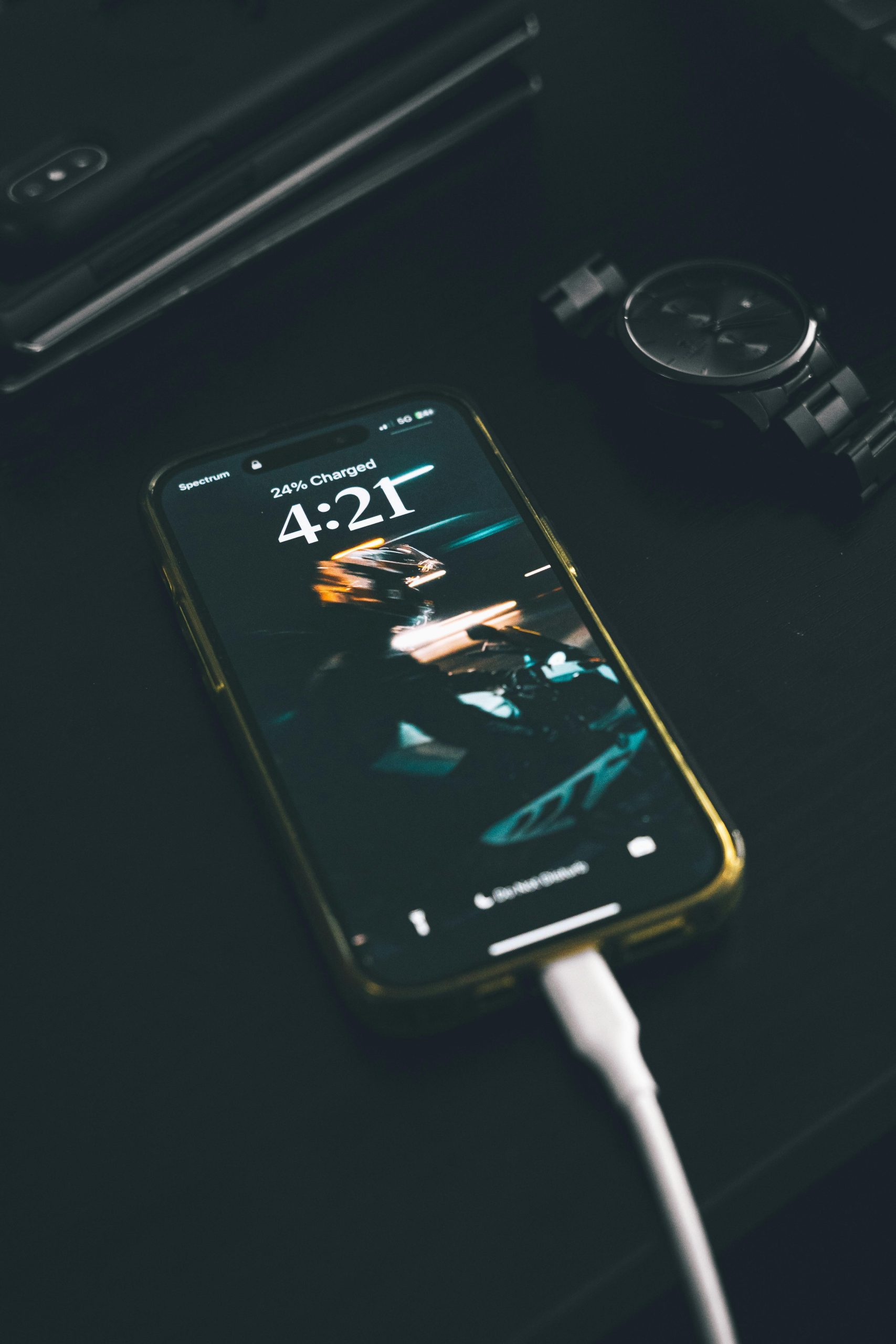Smartphone charging on a dark wooden table with a digital watch nearby. Un smartphone en charge sur une table en bois foncé avec une montre numérique à proximité.