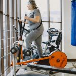 An adult woman using an elliptical trainer in a bright, modern gym. Une femme adulte utilisant un vélo elliptique dans une salle de sport moderne et lumineuse.