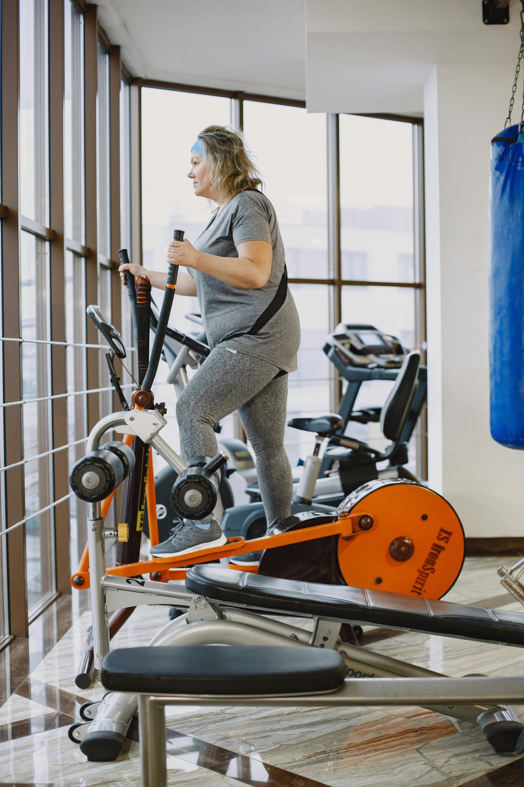 An adult woman using an elliptical trainer in a bright, modern gym. Une femme adulte utilisant un vélo elliptique dans une salle de sport moderne et lumineuse.