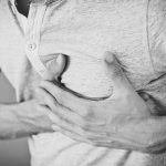 Black and white photo of a man clutching his chest, indicating discomfort or pain. Photo en noir et blanc d'un homme se tenant la poitrine, indiquant un inconfort ou une douleur.