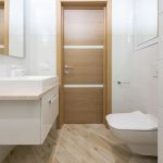 Modern timber door of contemporary clean new bathroom with mirrors and toilet on laminate --- Porte en bois moderne d'une salle de bain contemporaine propre et neuve avec miroirs et toilettes sur stratifié