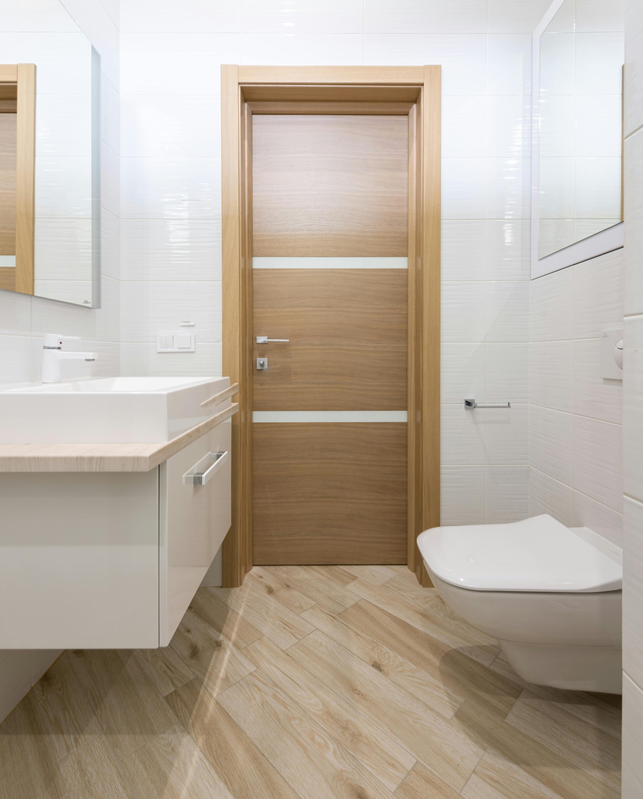 Modern timber door of contemporary clean new bathroom with mirrors and toilet on laminate --- Porte en bois moderne d'une salle de bain contemporaine propre et neuve avec miroirs et toilettes sur stratifié