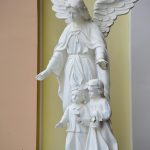 A serene white statue of an angel with two children, symbolizing protection. Une statue blanche sereine d'un ange avec deux enfants, symbolisant la protection.