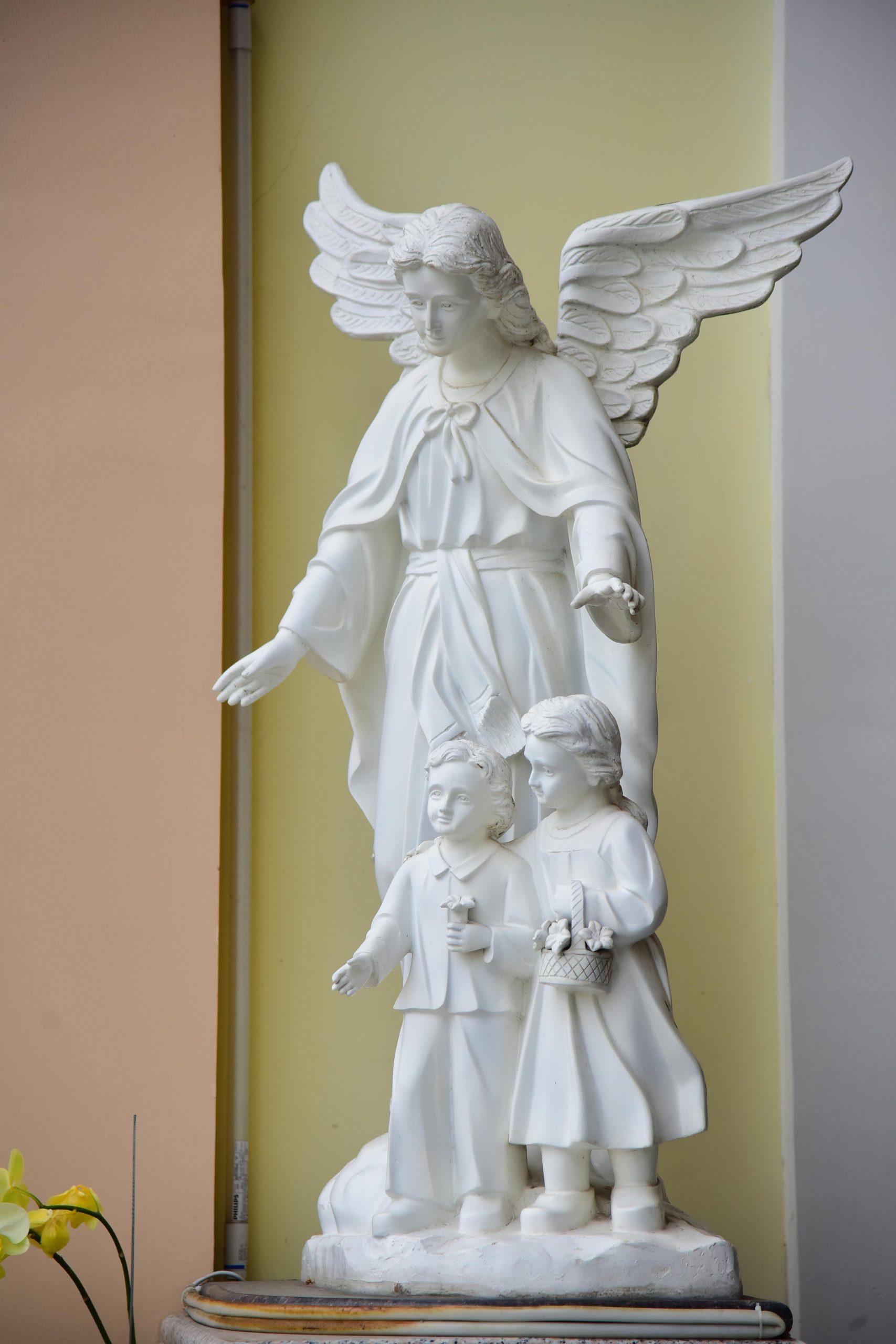 A serene white statue of an angel with two children, symbolizing protection. Une statue blanche sereine d'un ange avec deux enfants, symbolisant la protection.