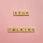Wooden Scrabble tiles on pink background spelling 'Stop Talking'. Tuiles de Scrabble en bois sur fond rose orthographiant « Stop Talking ».