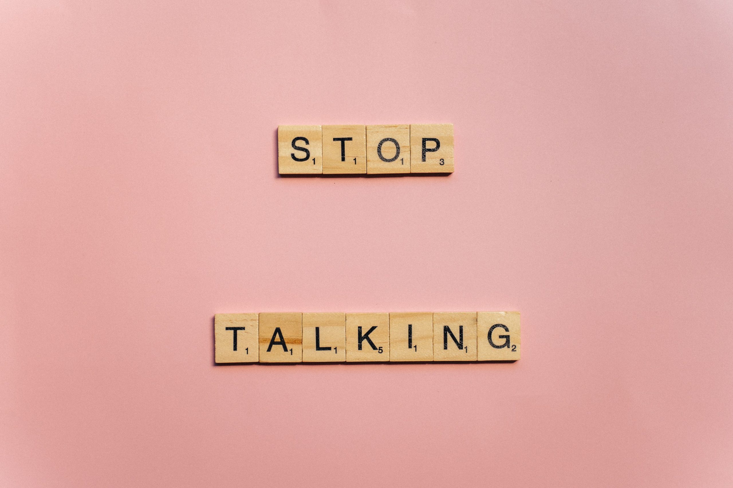 Wooden Scrabble tiles on pink background spelling 'Stop Talking'. Tuiles de Scrabble en bois sur fond rose orthographiant « Stop Talking ».