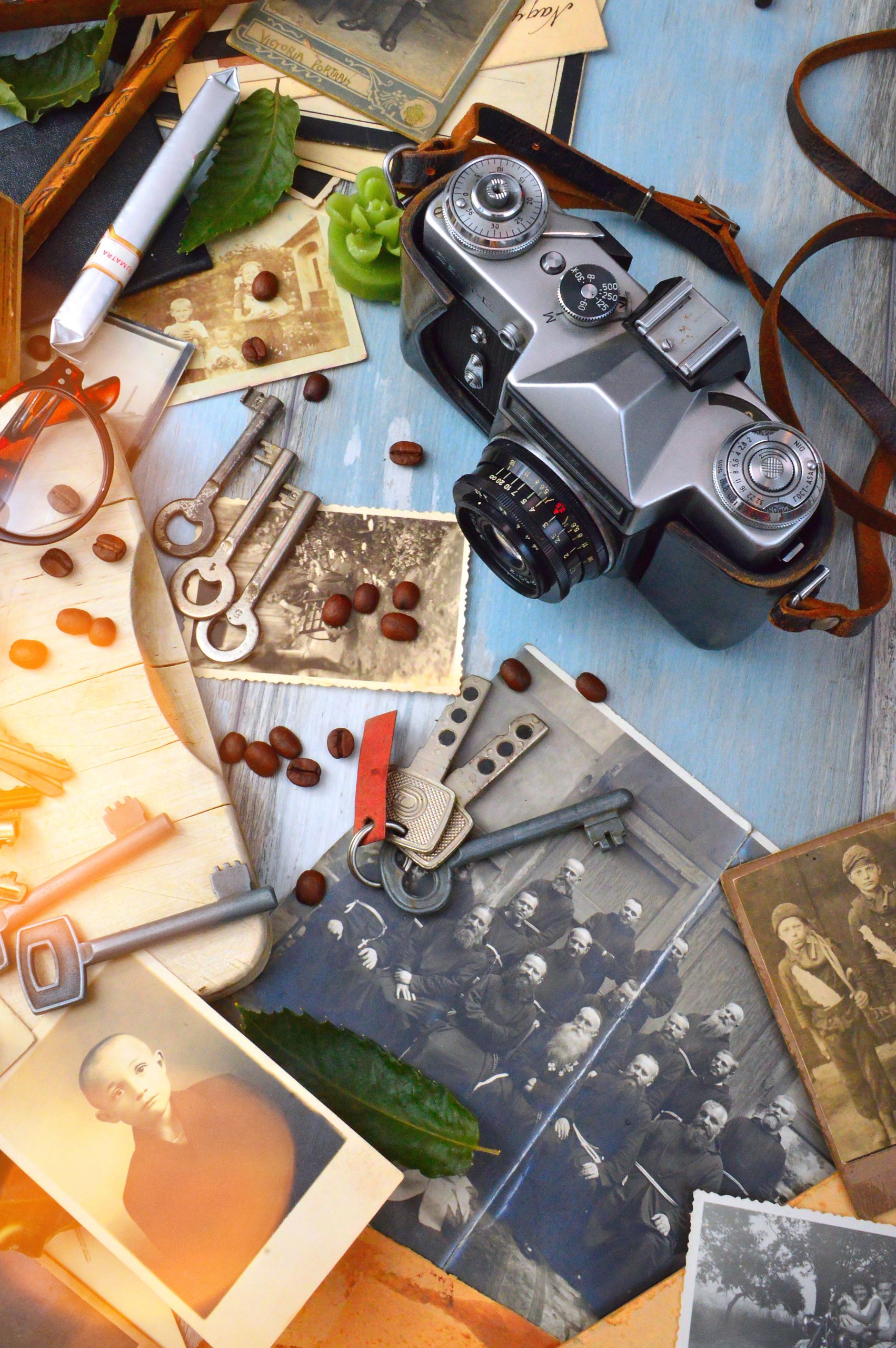 A flat lay of a vintage camera surrounded by old black and white photos, keys, and coffee beans. Une composition à plat d'un appareil photo vintage entouré de vieilles photos en noir et blanc, de clés et de grains de café.