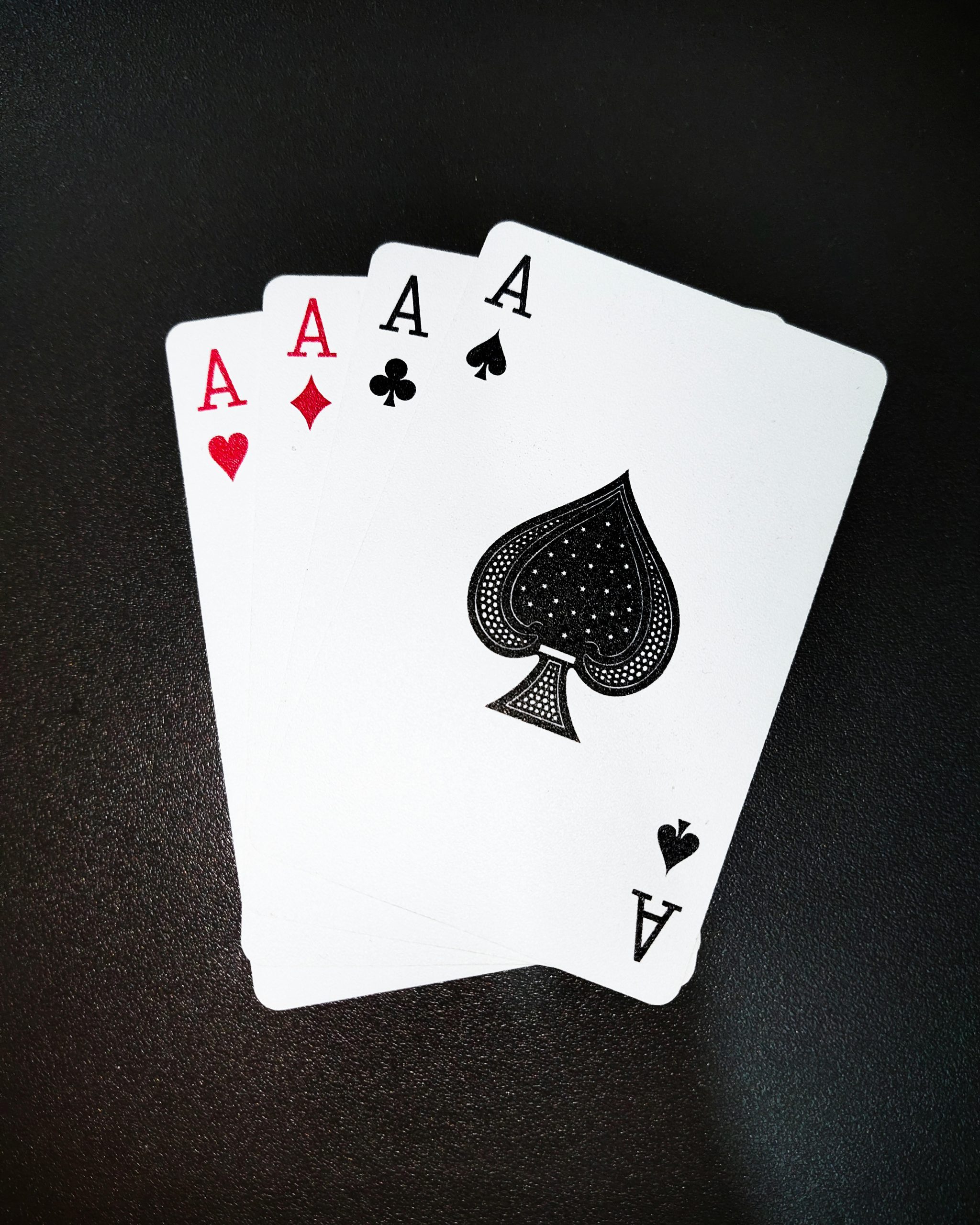 A close-up shot of four aces on a black background, showcasing symbols of poker and gambling. Gros plan de quatre as sur fond noir, mettant en évidence les symboles du poker et des jeux d'argent.