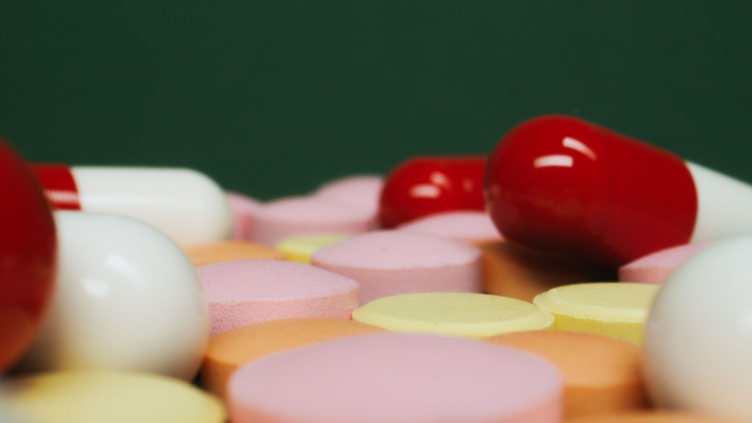 A close-up view of various colorful pills and tablets on a green background, focusing on medication variety. Une vue rapprochée de diverses pilules et comprimés colorés sur un fond vert, mettant l'accent sur la variété des médicaments.