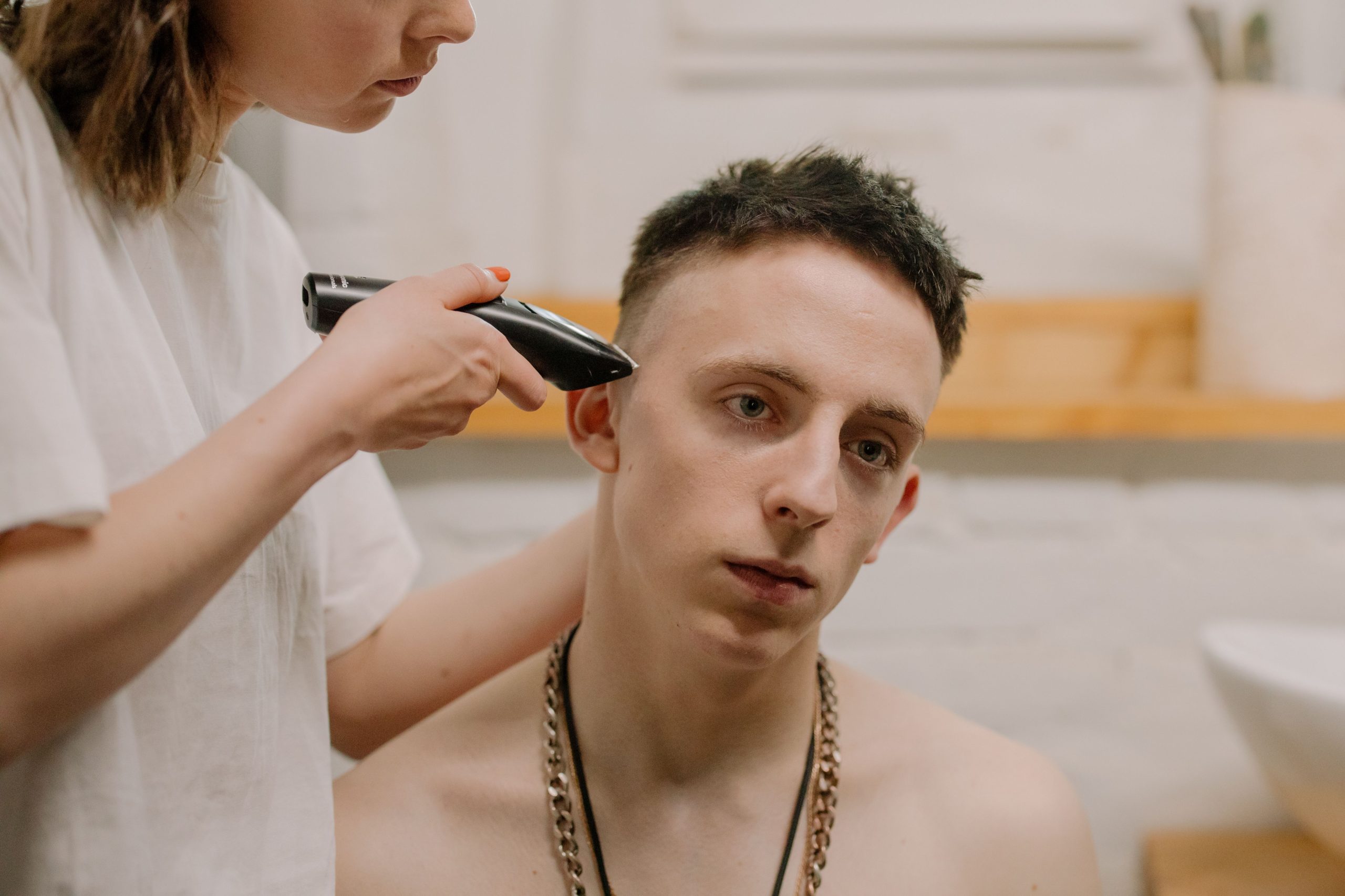 Jeune homme caucasien recevant une coupe de cheveux à domicile, coupé par une femme adulte à l'aide d'une tondeuse électrique.