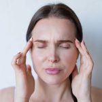 Femme les yeux fermés qui masse ses tempes pour calmer une douleur