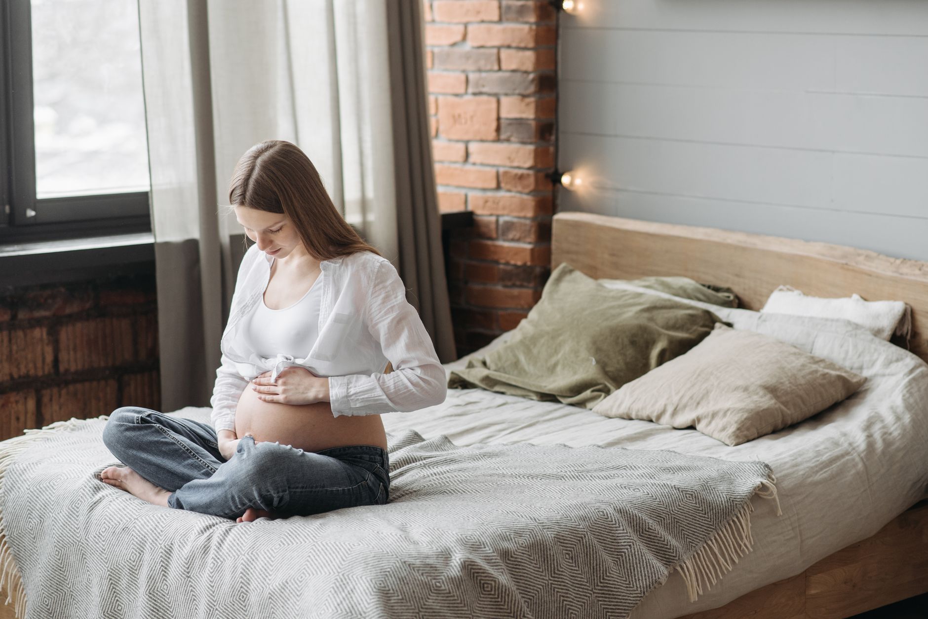 Future maman assise sur un lit, main sur le ventre