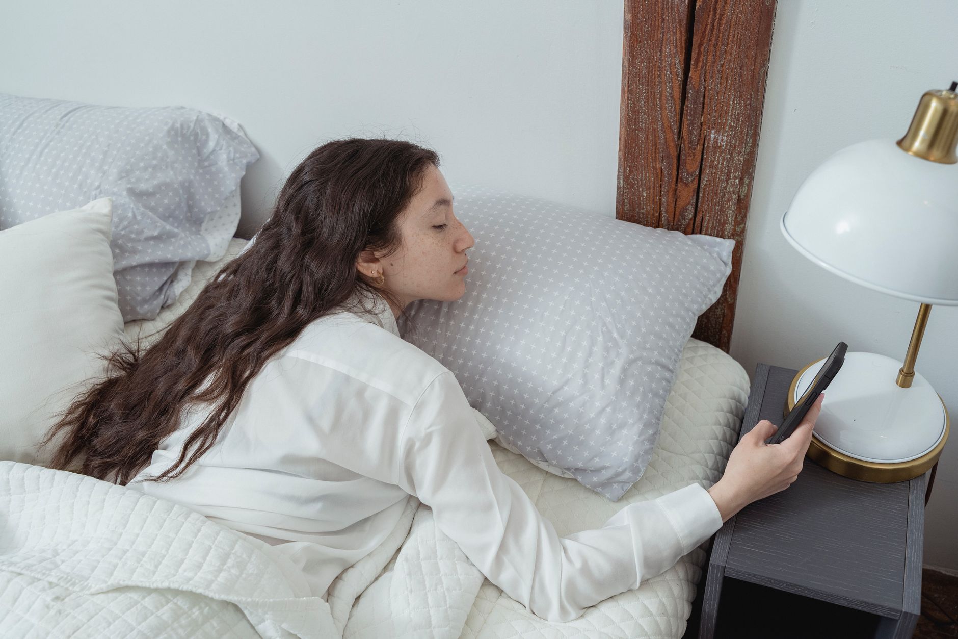 Jeune femme au lit consultant son téléphone sous la couette